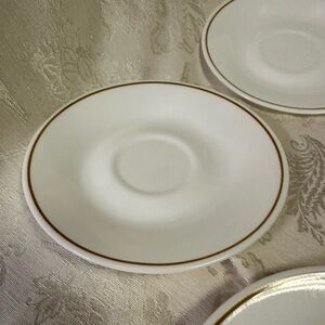 Five 6 1/8” Sand Art Peach Saucers. By Corning white with orange trim.